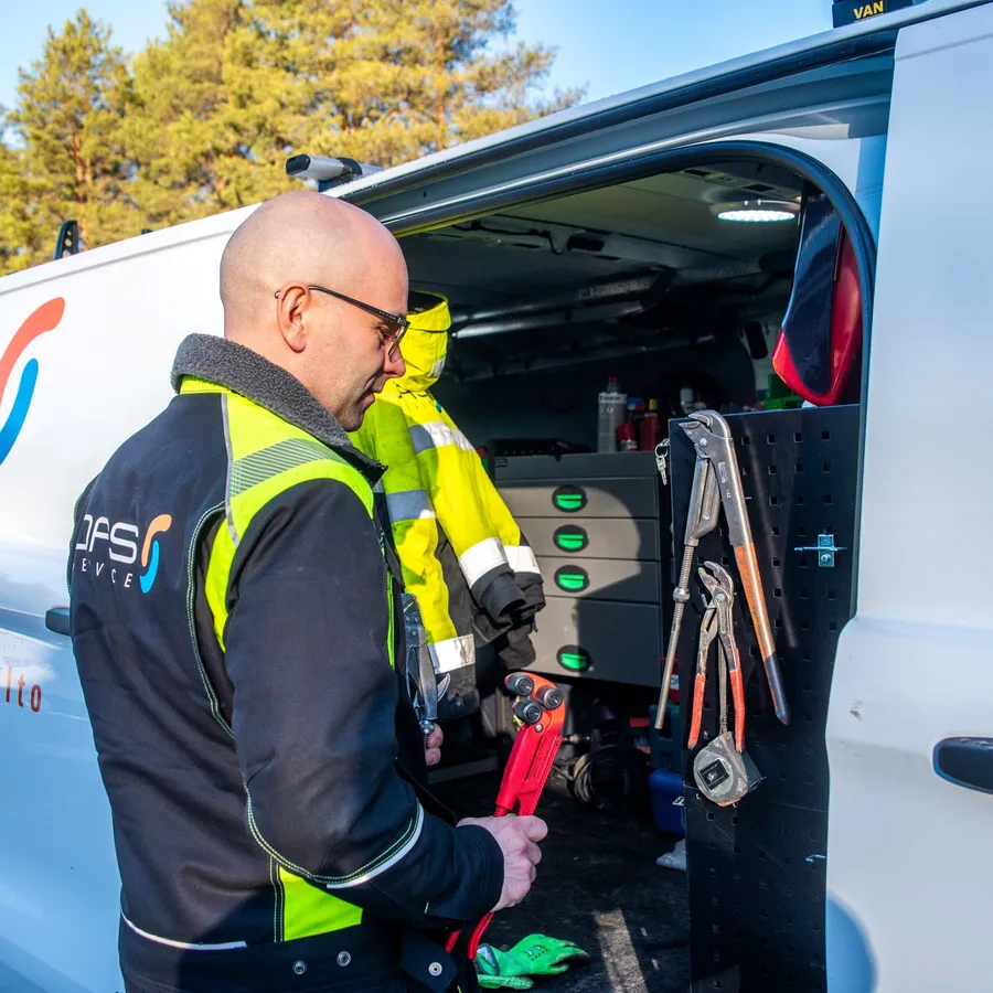 Sähköasentaja työskentelee huoltoauton takana ja valmistelee työkaluja asennustehtävään kirkkaana talvipäivänä.