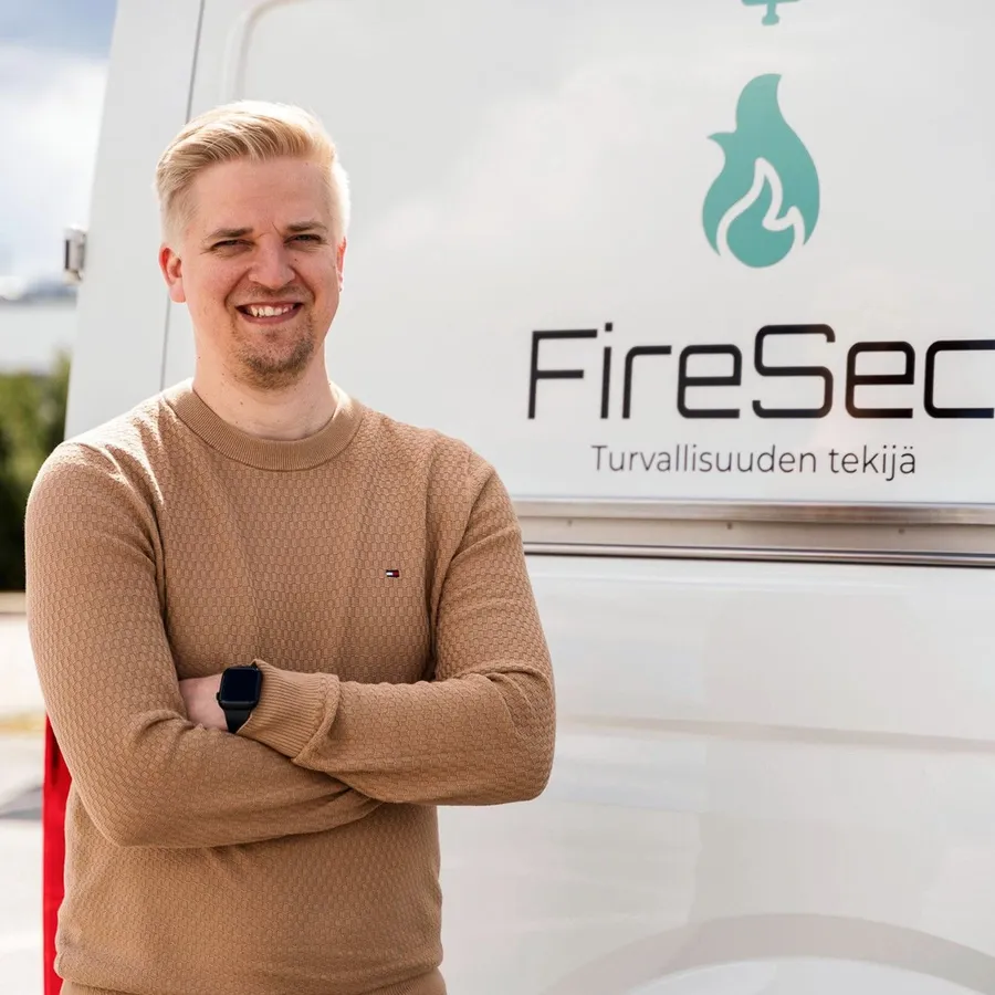 Hymyilevä mies seisoo hyötyajoneuvon edessä, jossa lukee teksti FireSec. 