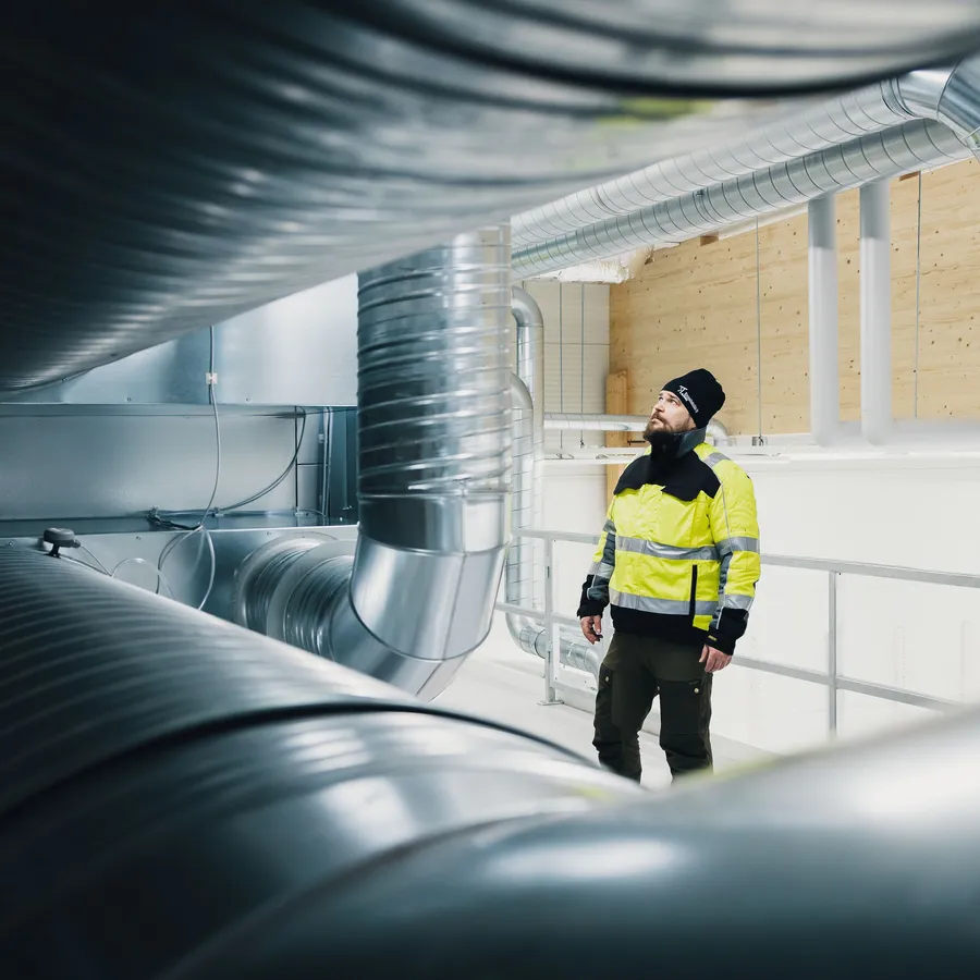 Rakennustekniikan ammattilainen tarkastaa suuria ilmanvaihtokanavia teollisuusrakennuksessa.